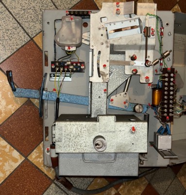 Vnitřek telefonního automatu, mincová dráha z pravého horního rohu středem nad kasičku, chybí korýtko (vlevo přes vidlici) pro vracení minci do dvířek