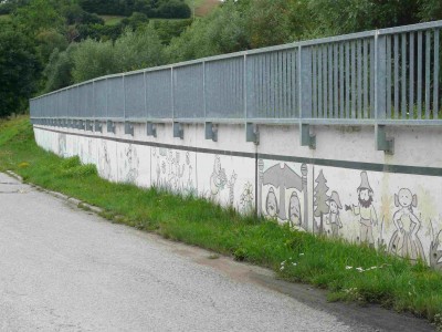 Zatáčka na cyklostezce s opěrnou zdí.
<br />Pohled ze souběžné vozovky - konec